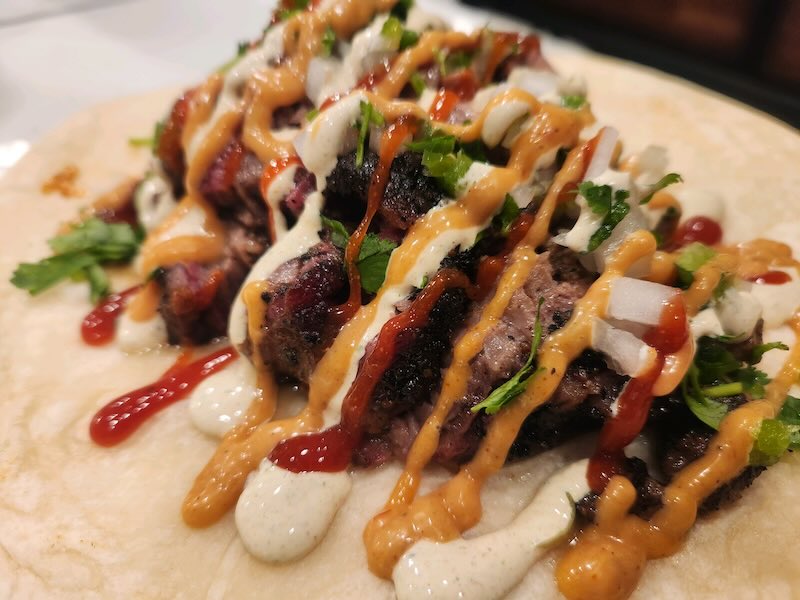 An unwrapped burrito filled with meat, veggies, and sauce